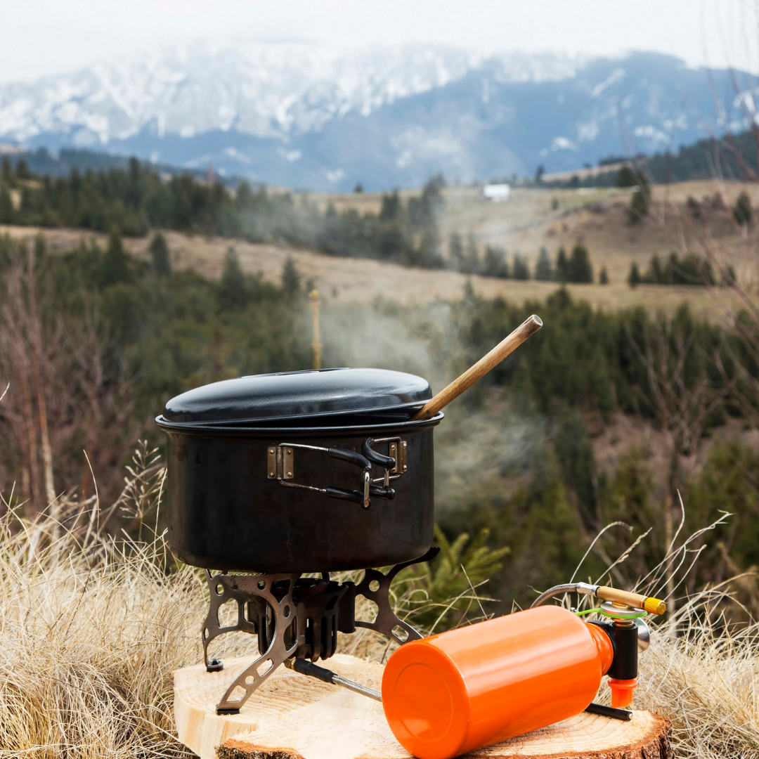 Portable cooking pot on a stove outdoors with snow-capped mountains in the background.